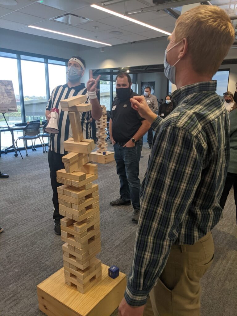 HAWA staff stand around a Jenga tower in a room with other students and mentors.